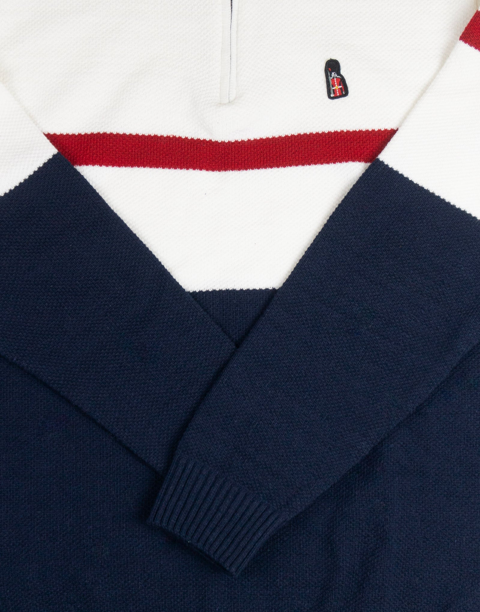 Navy sweater with a white collar and red stripe, featuring a logo on the chest.