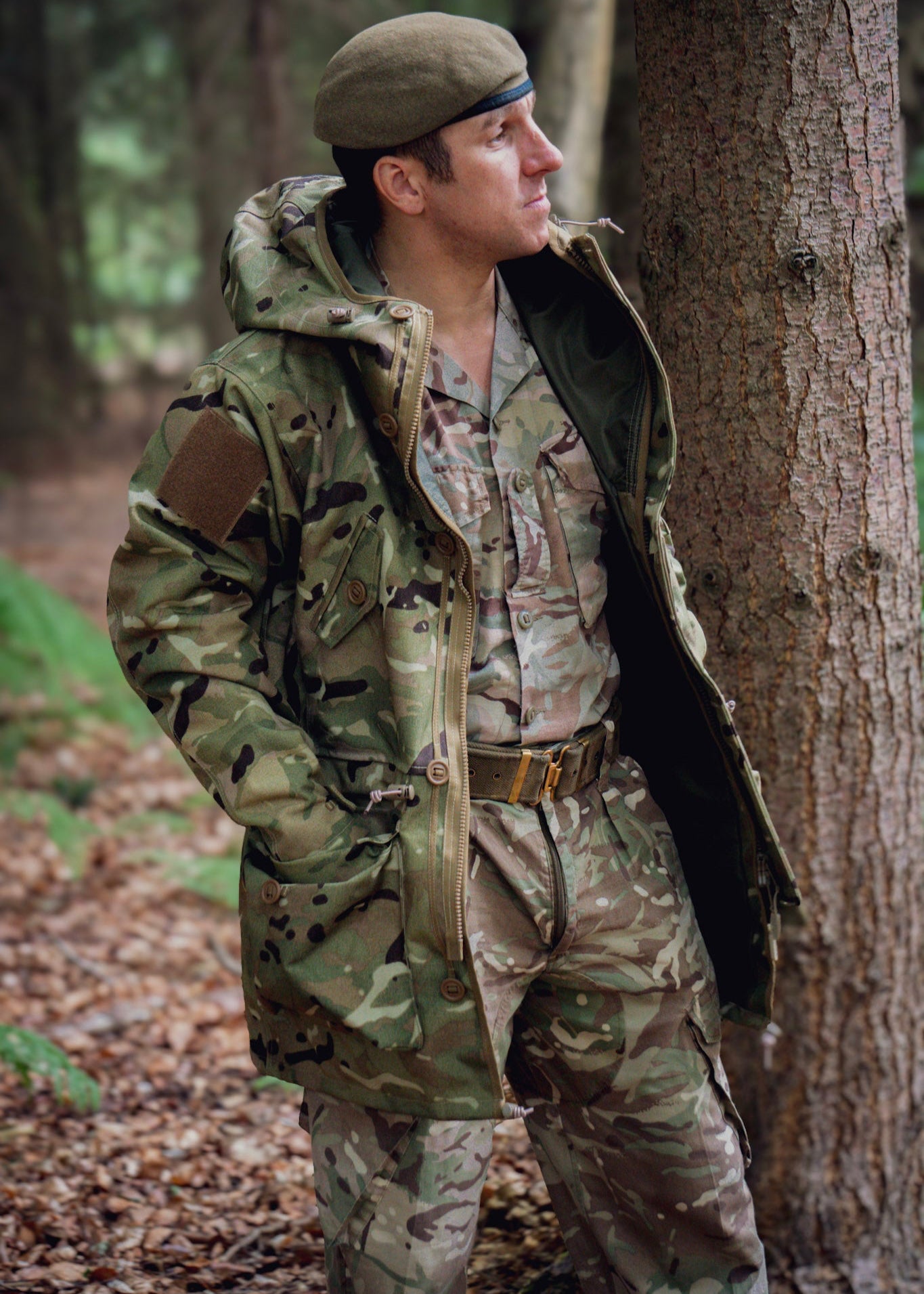 Person in camouflage uniform and waterproof coat standing in a forest