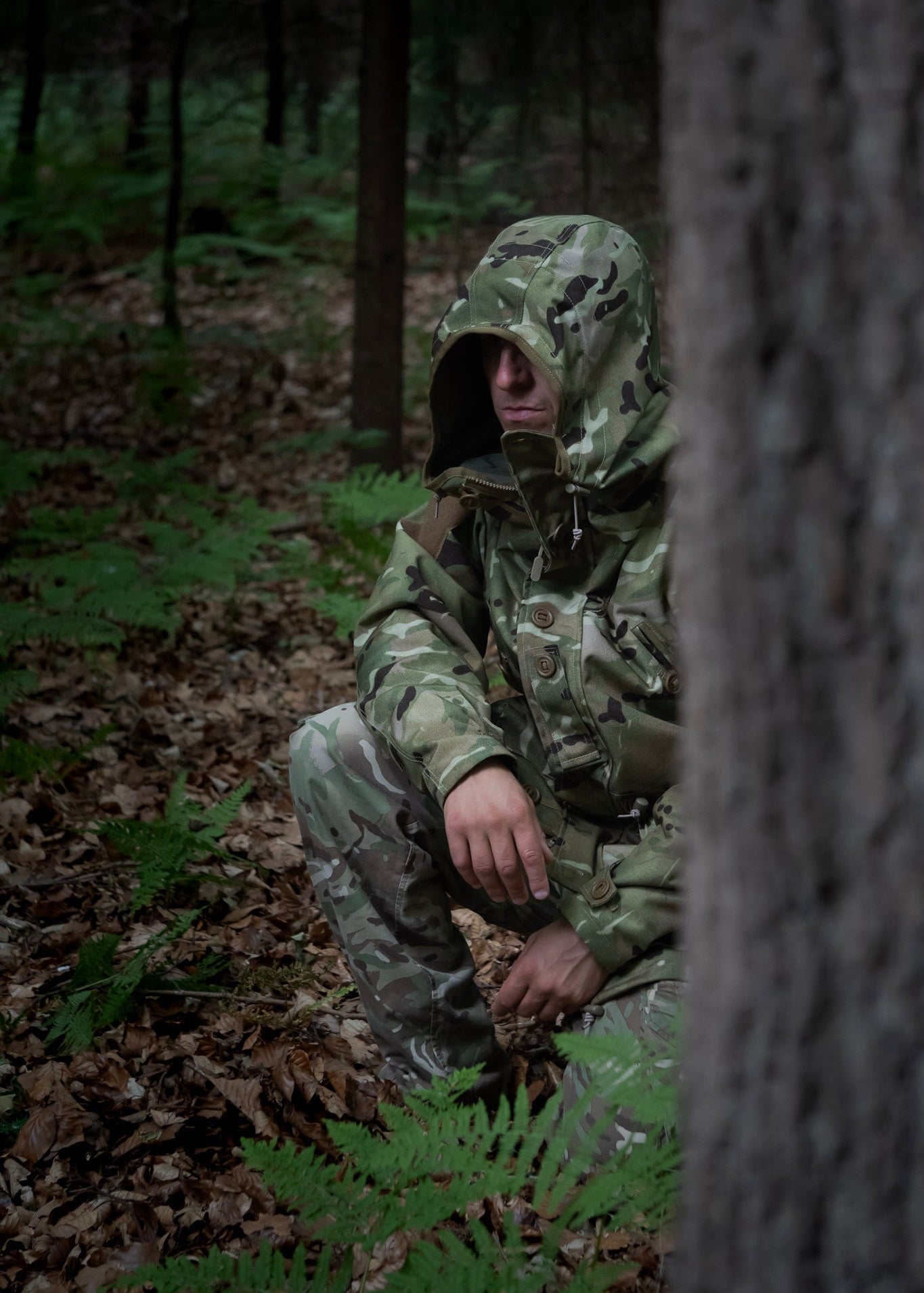 Person in camouflage gear crouching in a forest