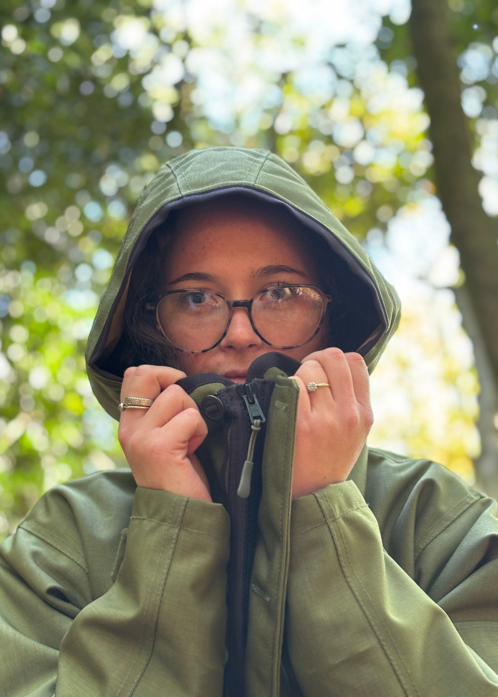 woman pulling the hood of green waterproof jacket around her face