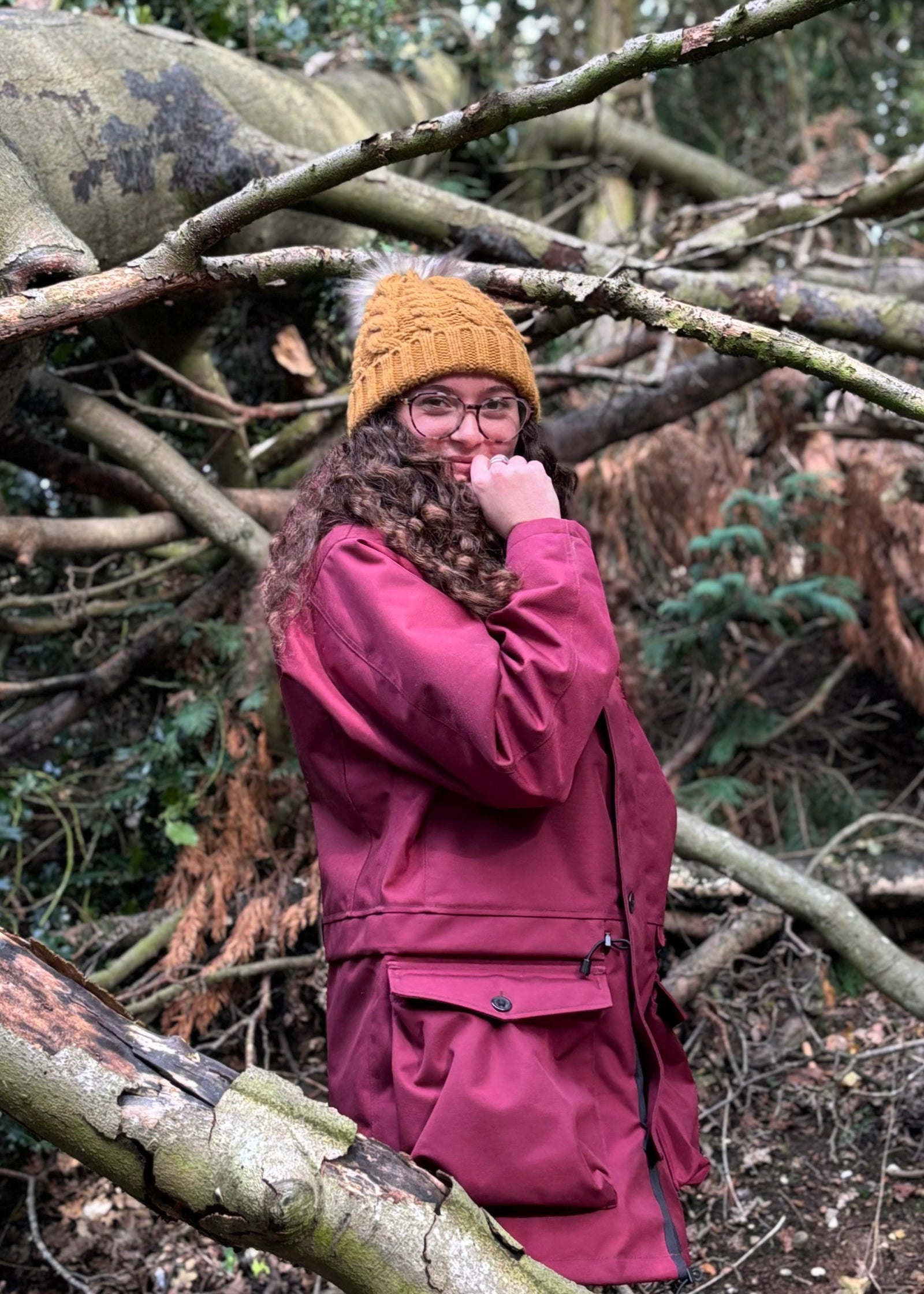woman stood by a collapsed tree smiling while wearing a re waterproof jacket and yellow hat