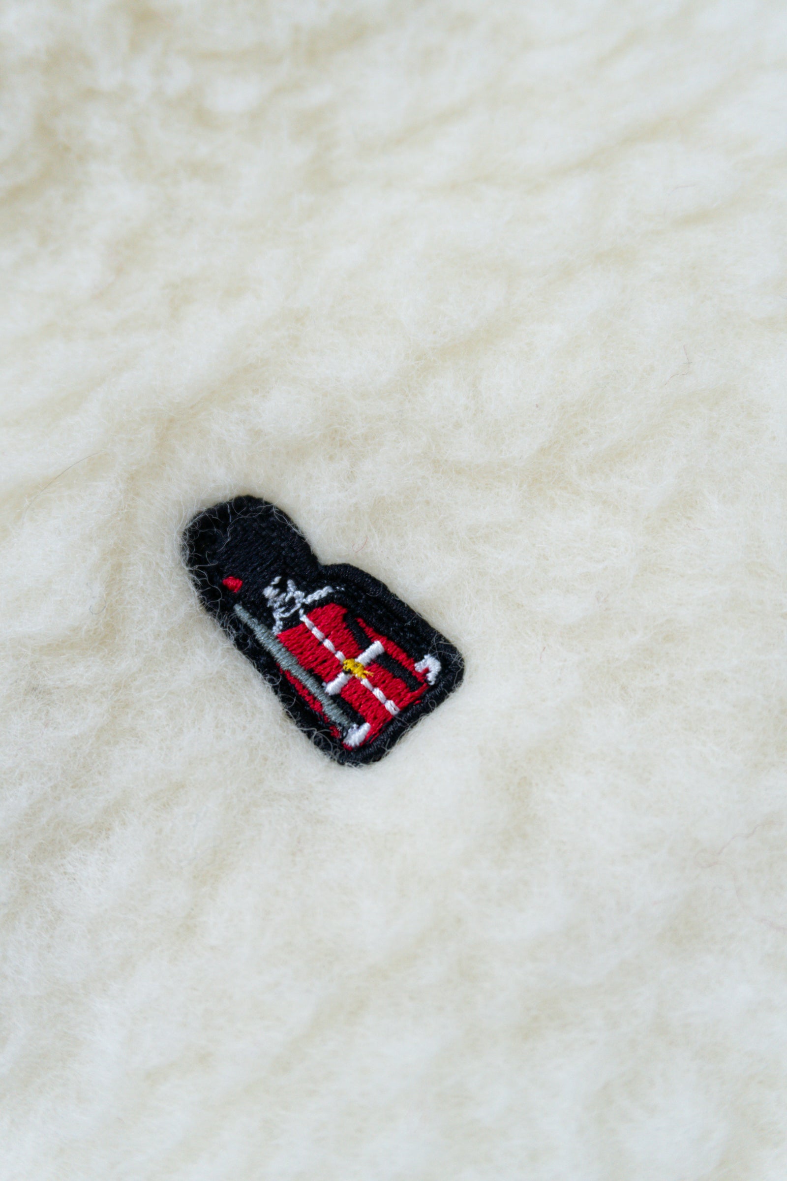Embroidered patch of a bottle with a red label on a textured white fabric background