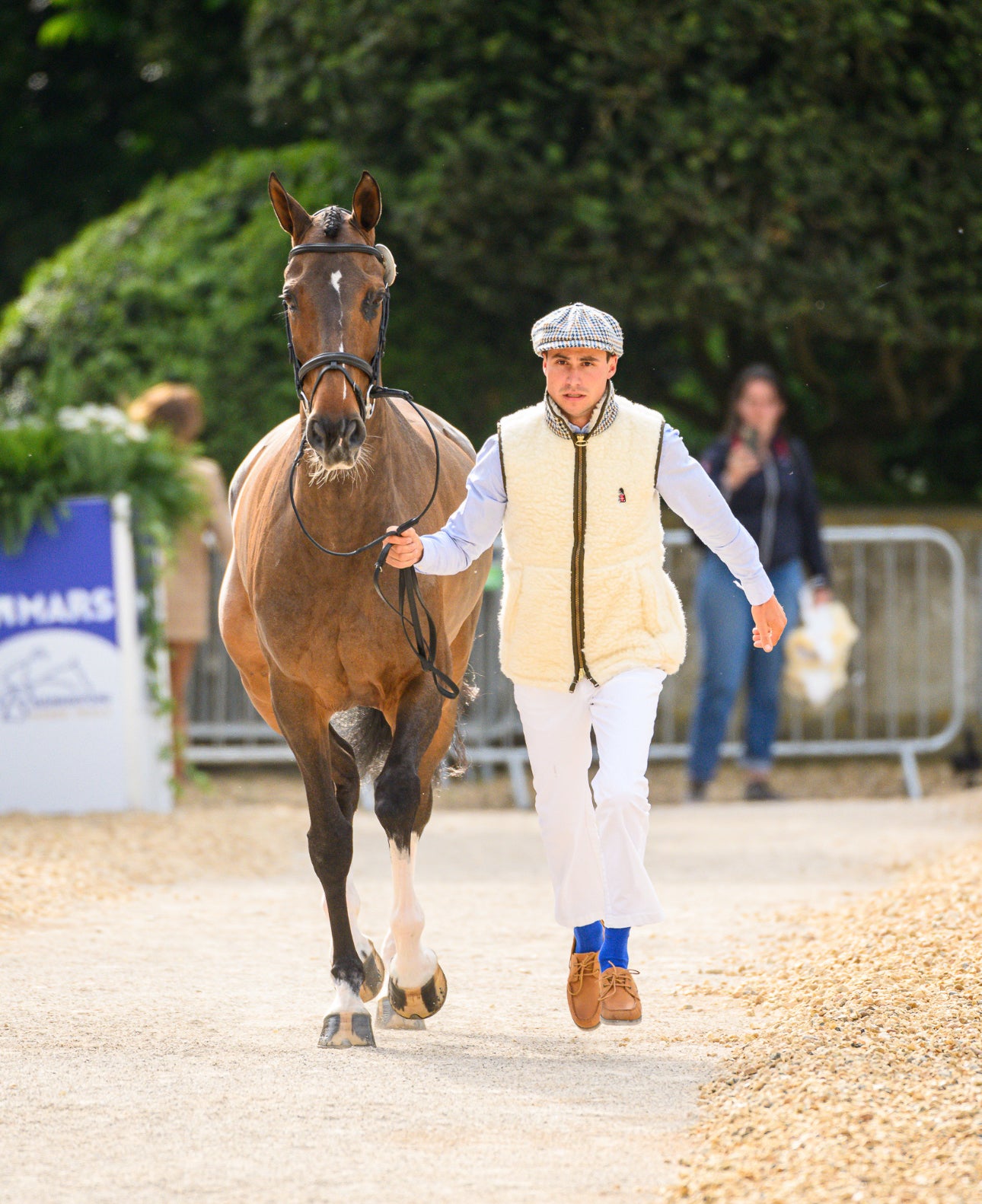 Person walking a horse on a gravel path with greenery in the background