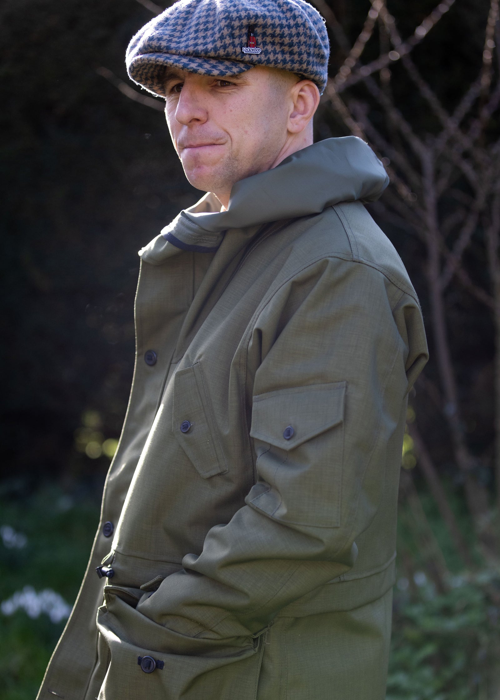green waterproof jacket with multiple pockets and grey tweed flat cap