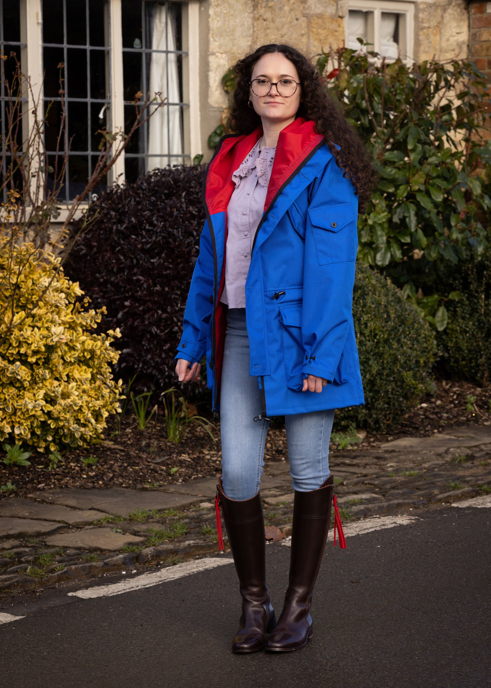 woman wearing a blue waterproof jacket with a red lining walking down a street in a country town