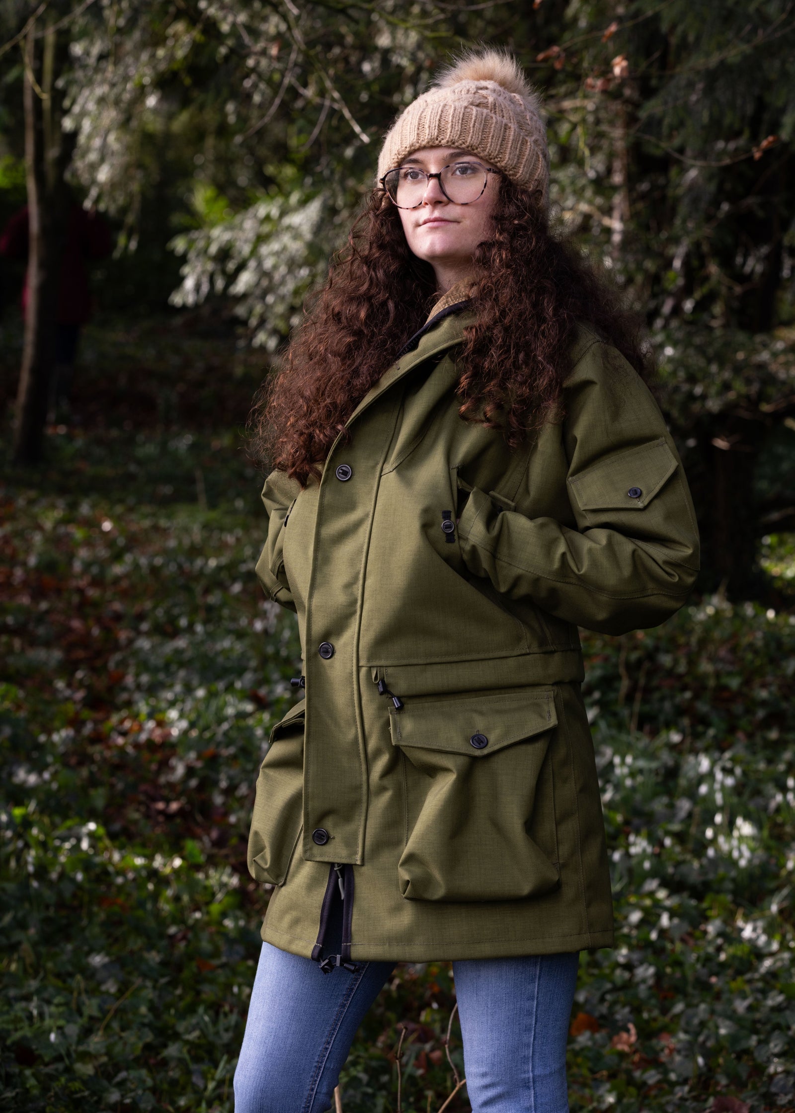 A person wearing a green waterproof Churchill smock with multiple pockets, standing outdoors.