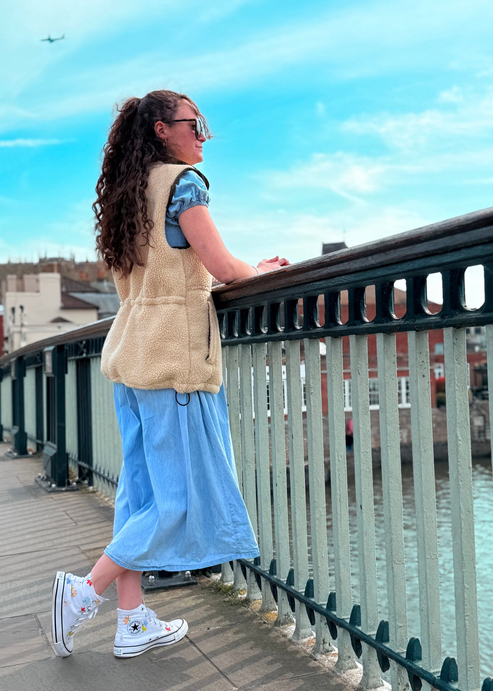 woman standing on a bridge wearing a blue dress and a beige gilet
