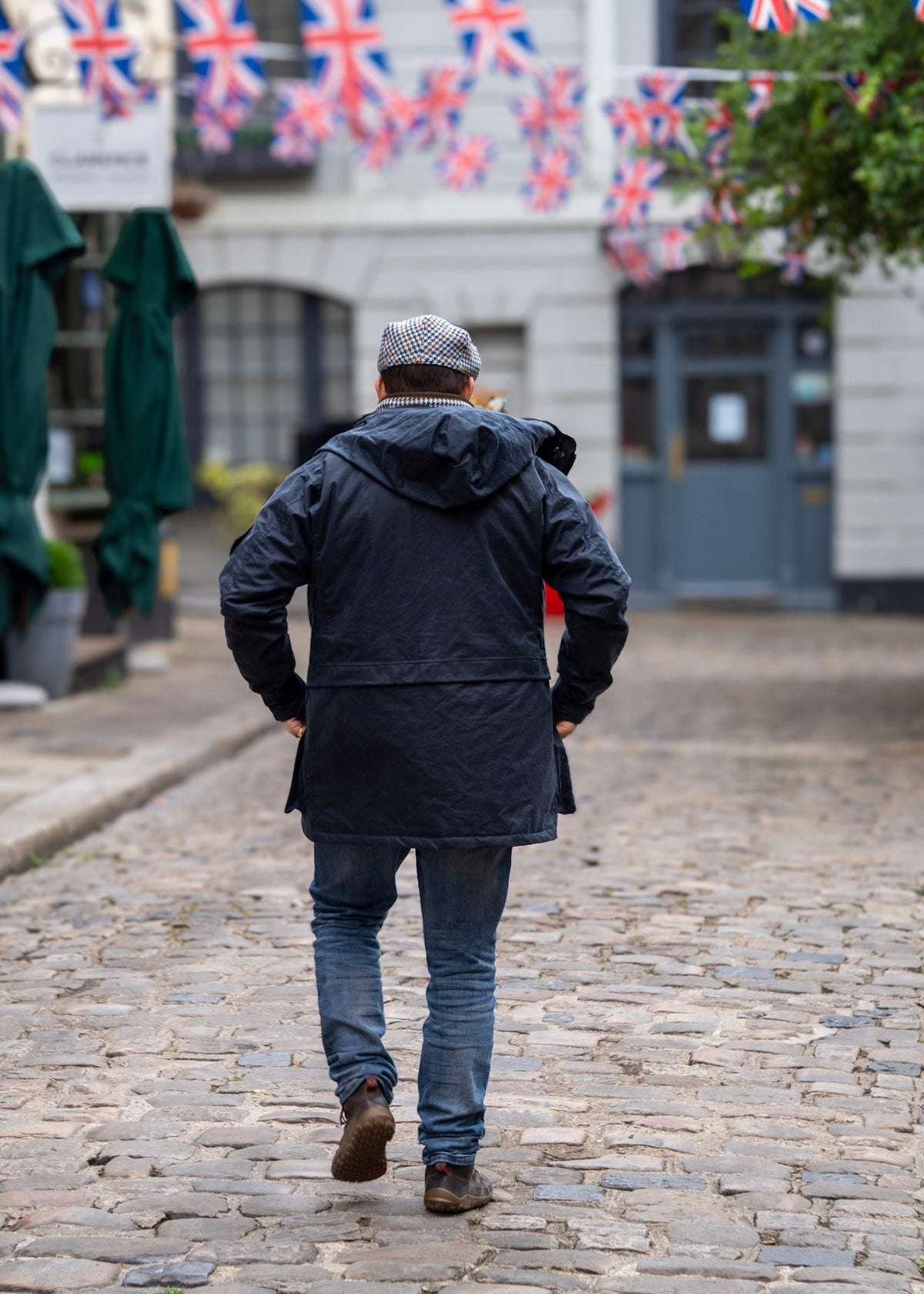 Man walking on a cobblestone street with British flags in the background wearing a wax jacket