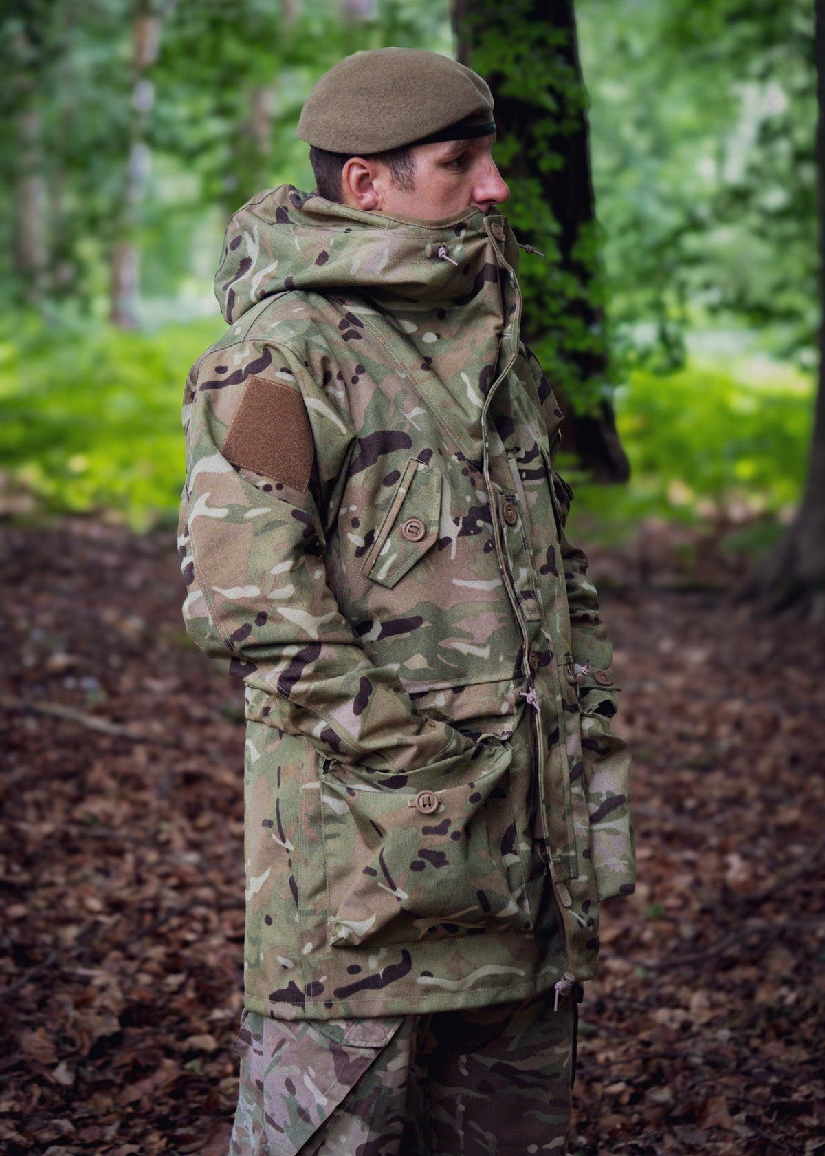 Person wearing a camouflage jacket and beret standing in a forest.