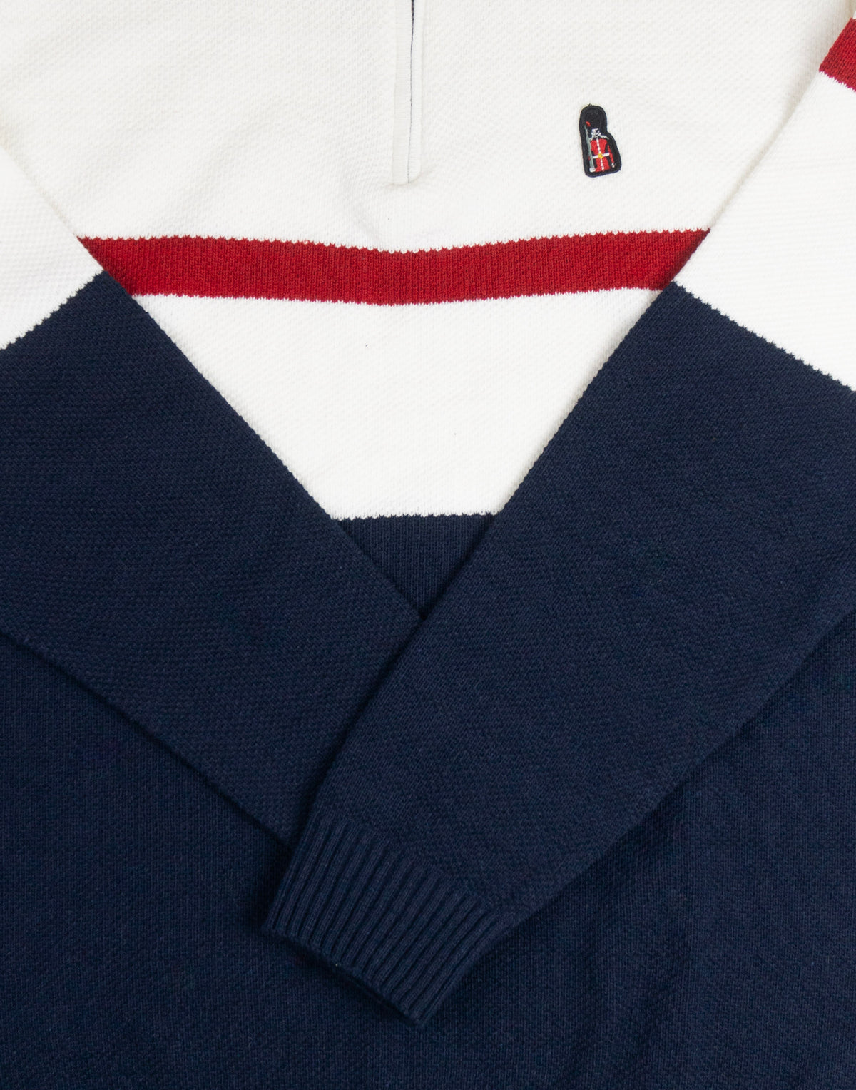 Navy sweater with a white collar and red stripe, featuring a logo on the chest.