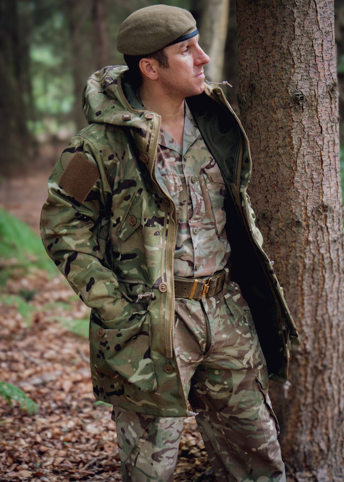 Person in camouflage uniform and waterproof coat standing in a forest