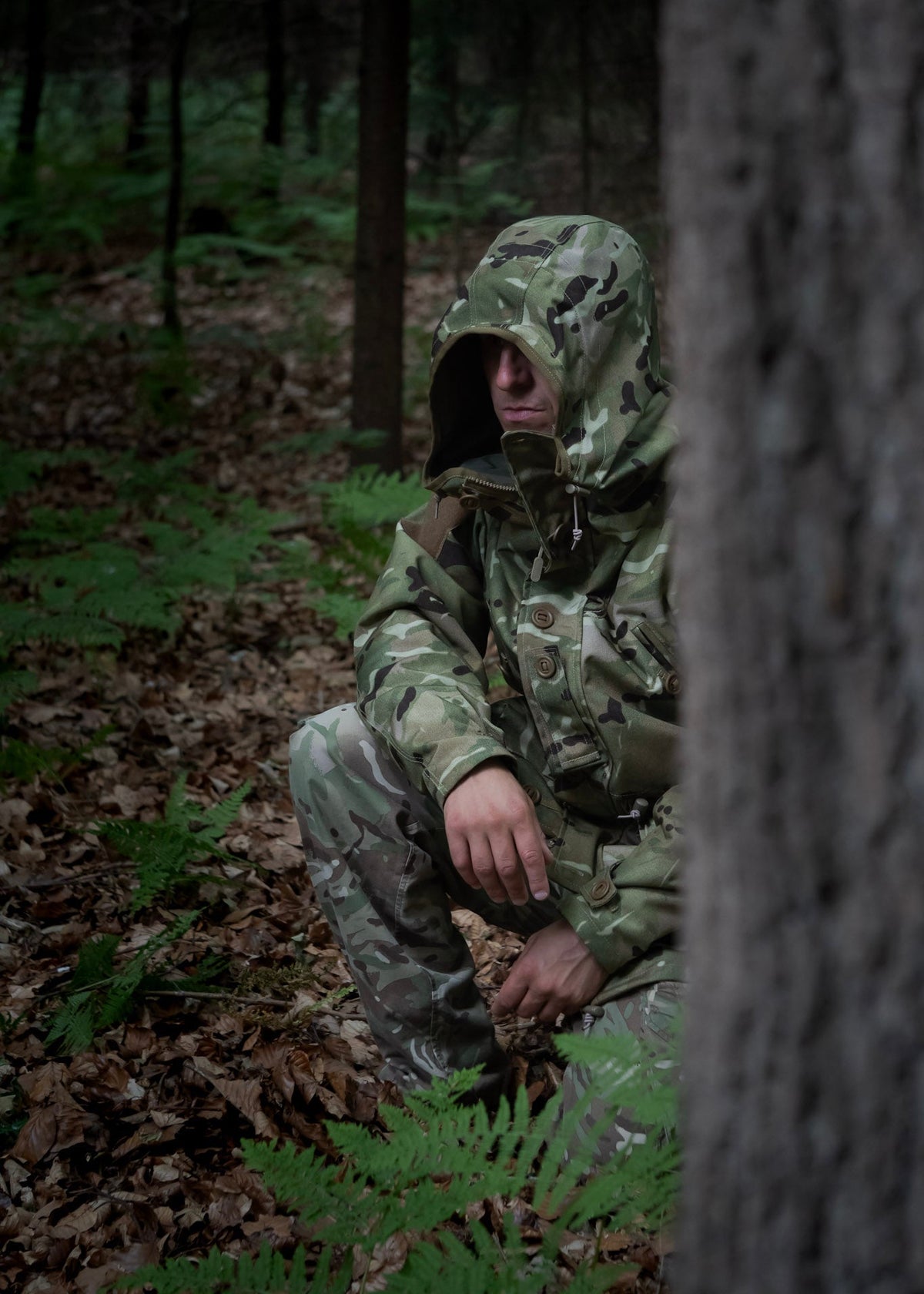 Person in camouflage gear crouching in a forest