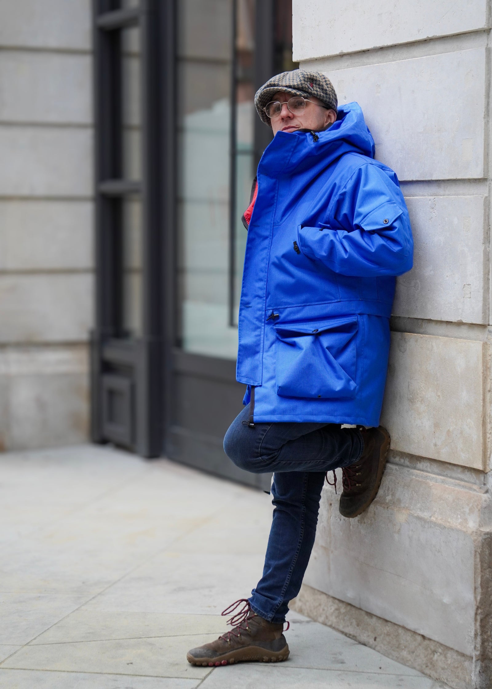 A person wearing a bold royal blue outer smock with red lining, standing against a wall.
