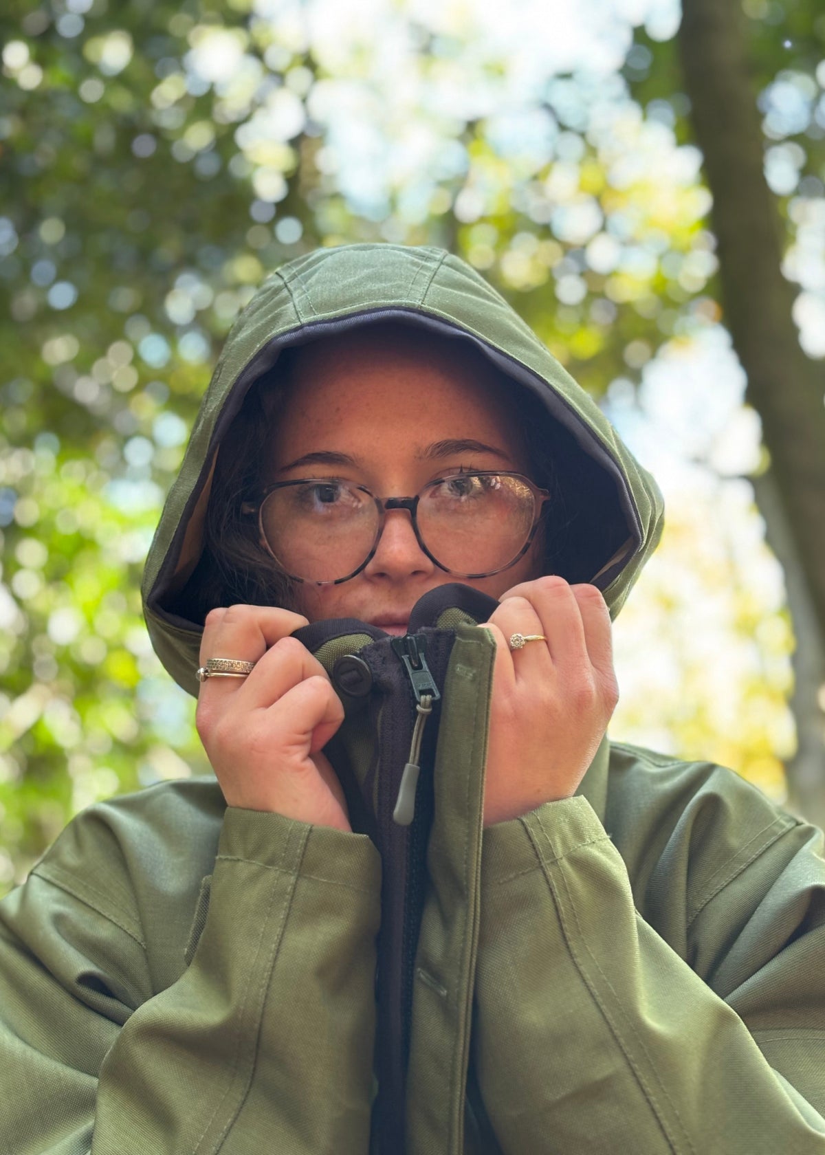 woman pulling the hood of green waterproof jacket around her face