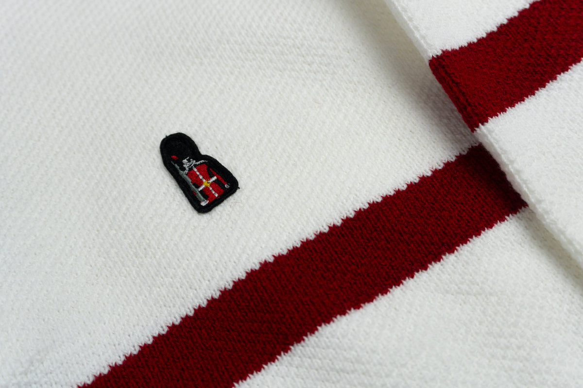 Close-up of a white sweater with red stripes and a small black and red emblem.