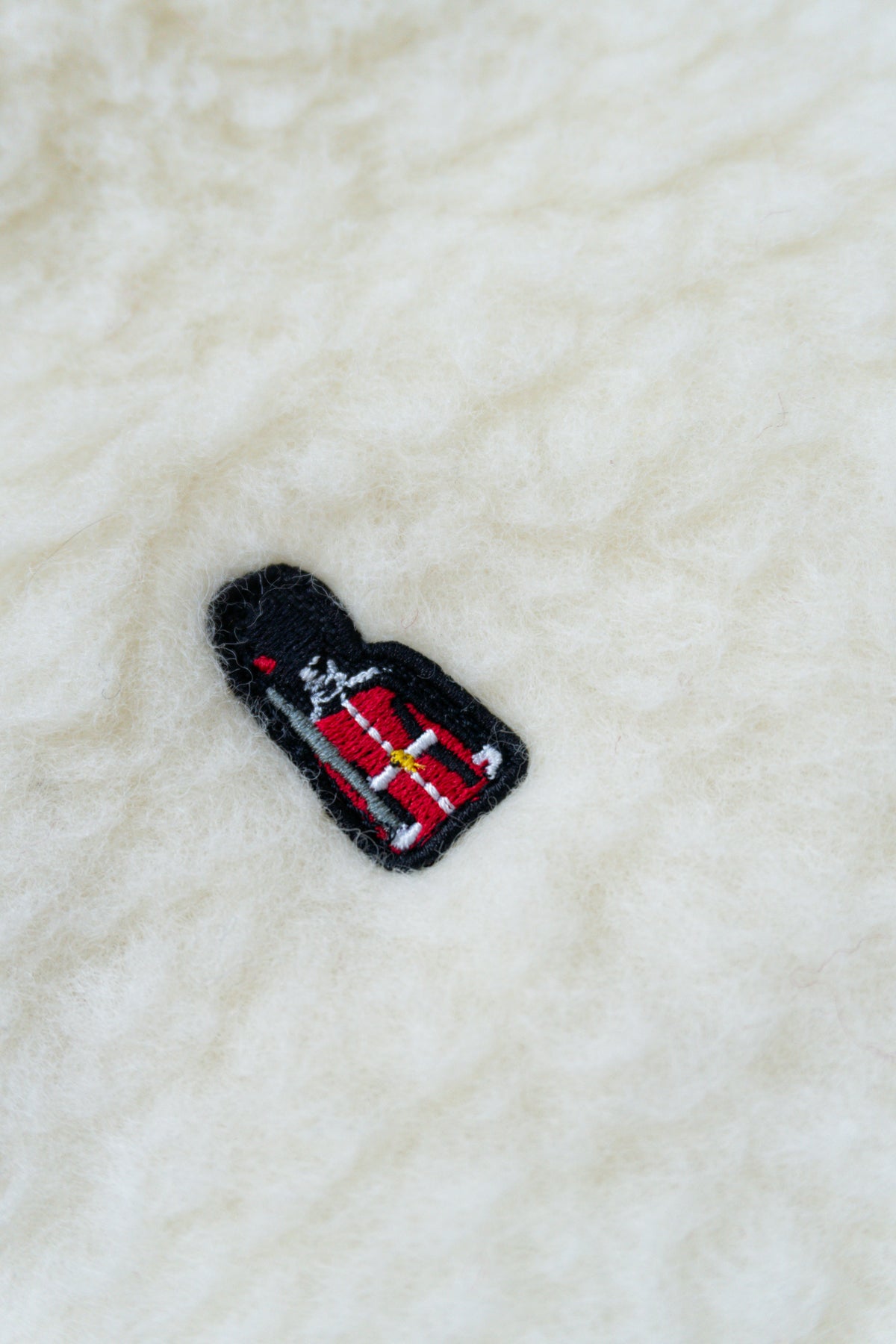 Embroidered patch of a bottle with a red label on a textured white fabric background