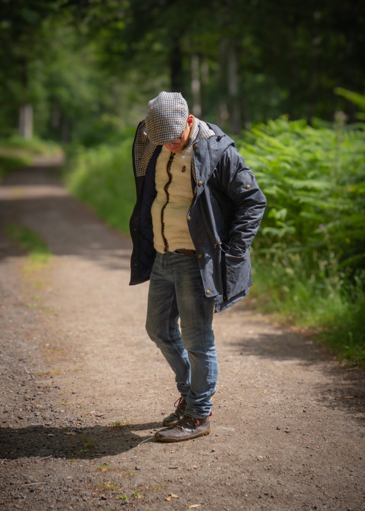 Person walking on a path in a forested area wearing a wax jacket and wool gilet