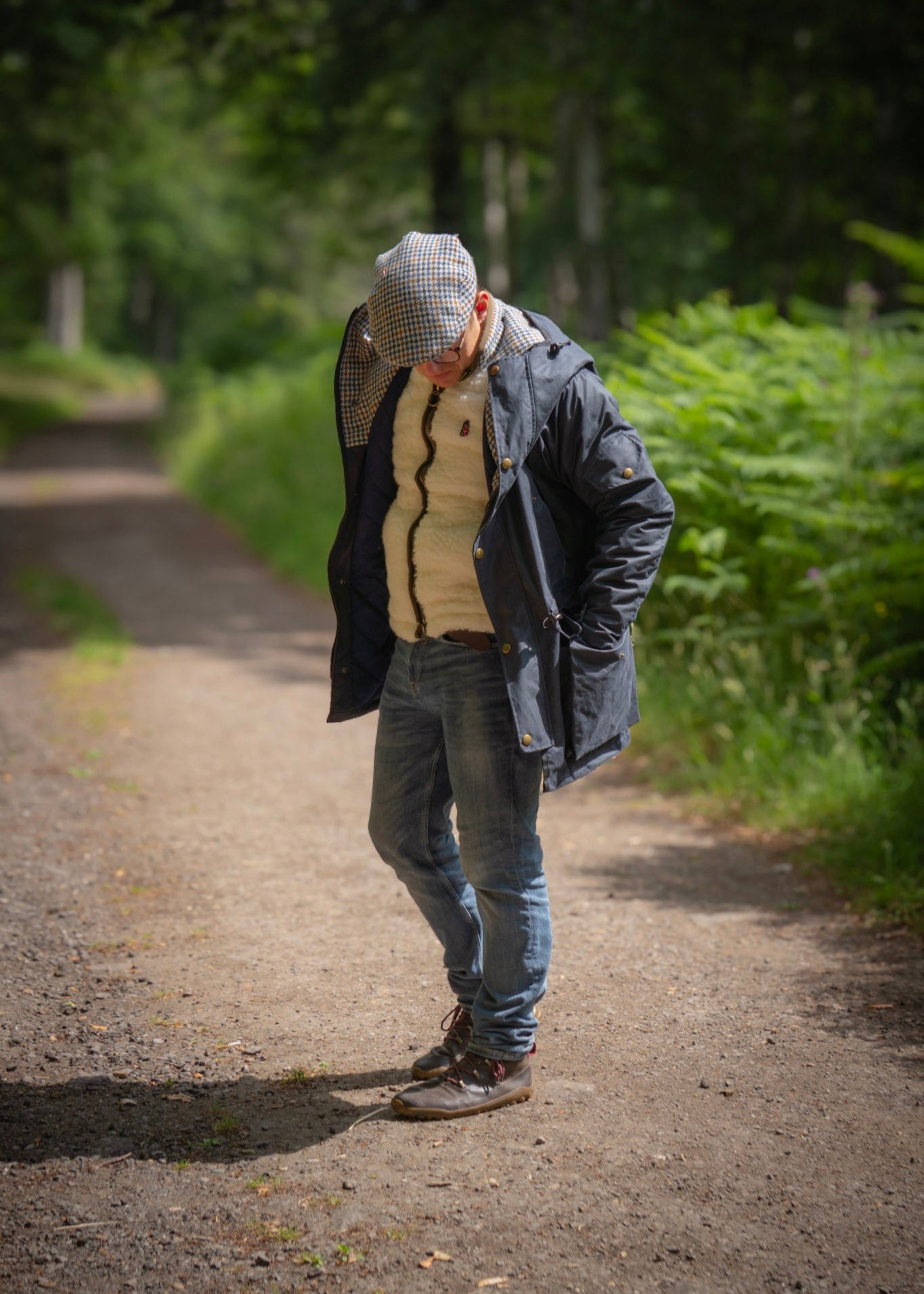 Person walking on a path in a forested area wearing a wax jacket and wool gilet