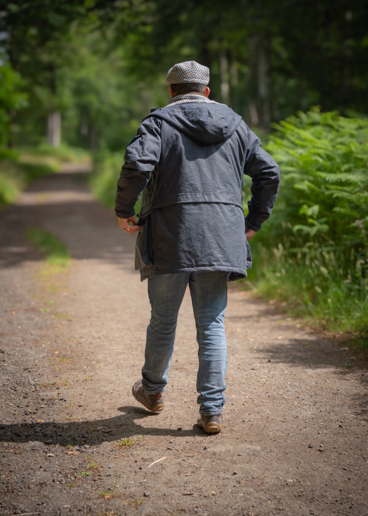 Person walking away on a path in a forest, wearing a wax jacket