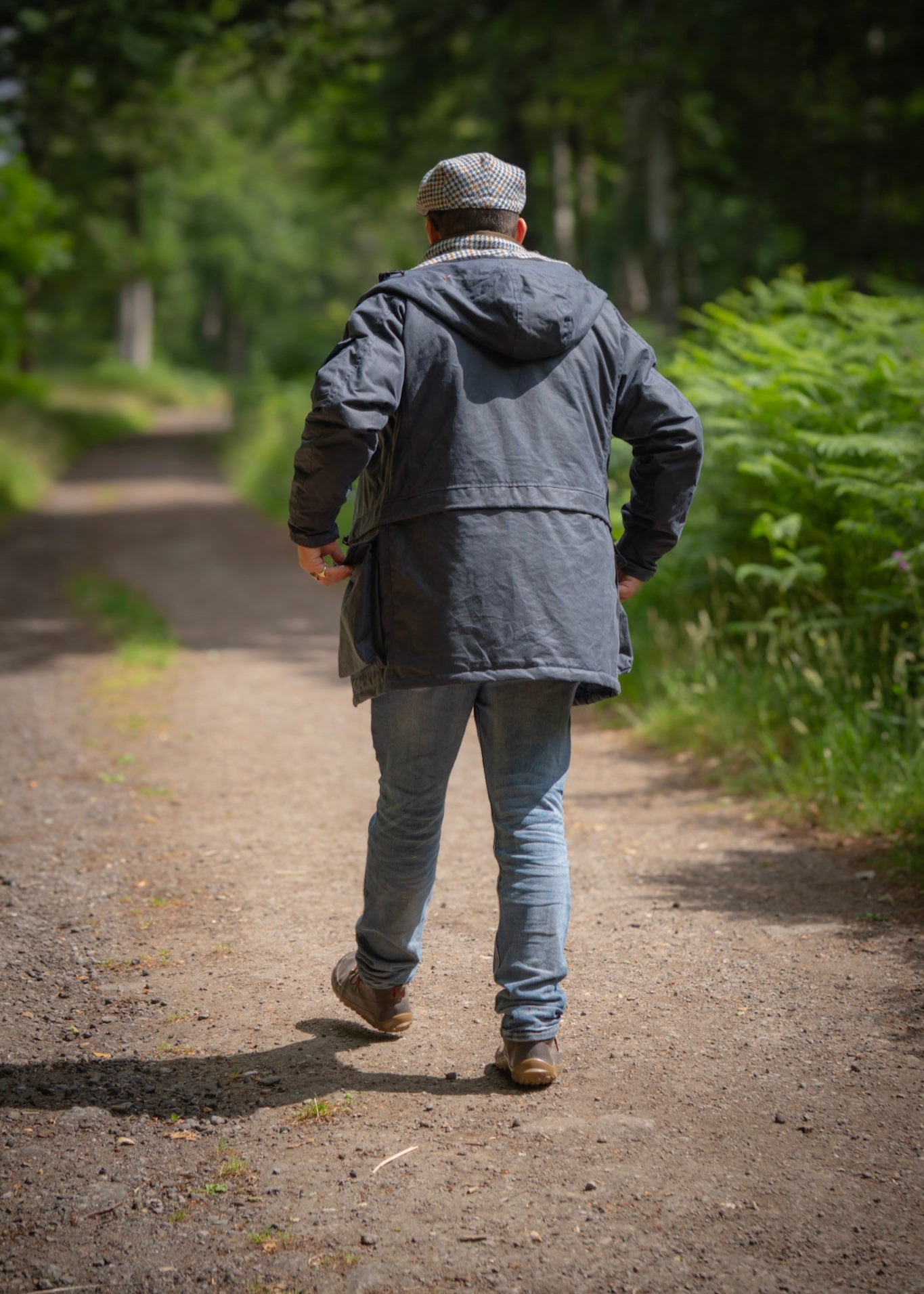 Person walking away on a path in a forest, wearing a wax jacket