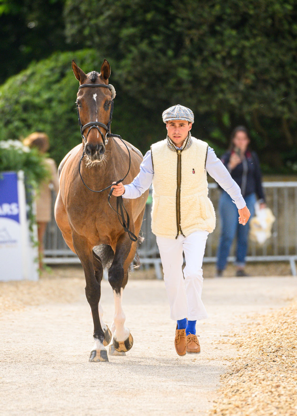Person walking a horse on a gravel path with greenery in the background