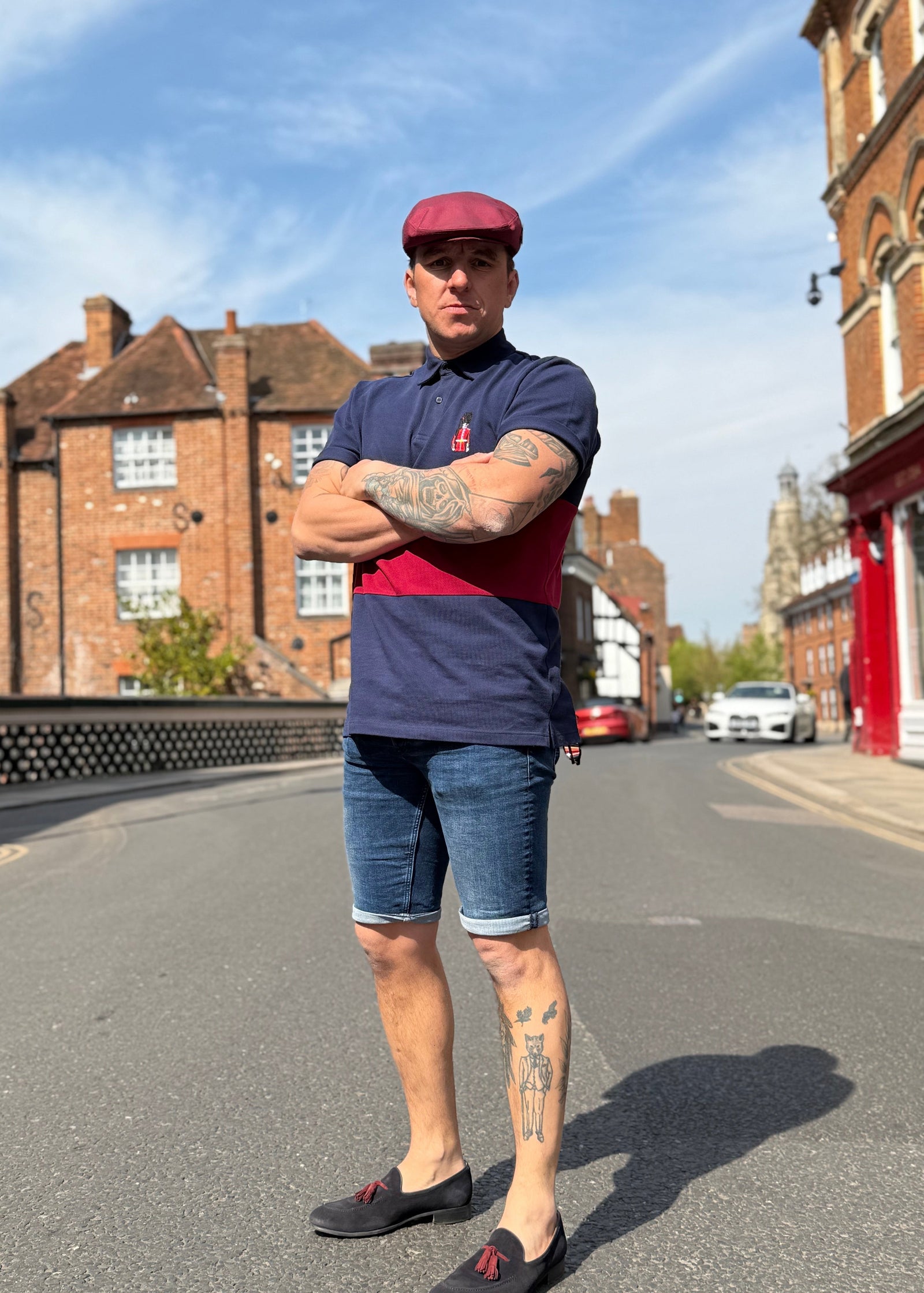 man stood in the street wearing a red cap and blue and red polo top