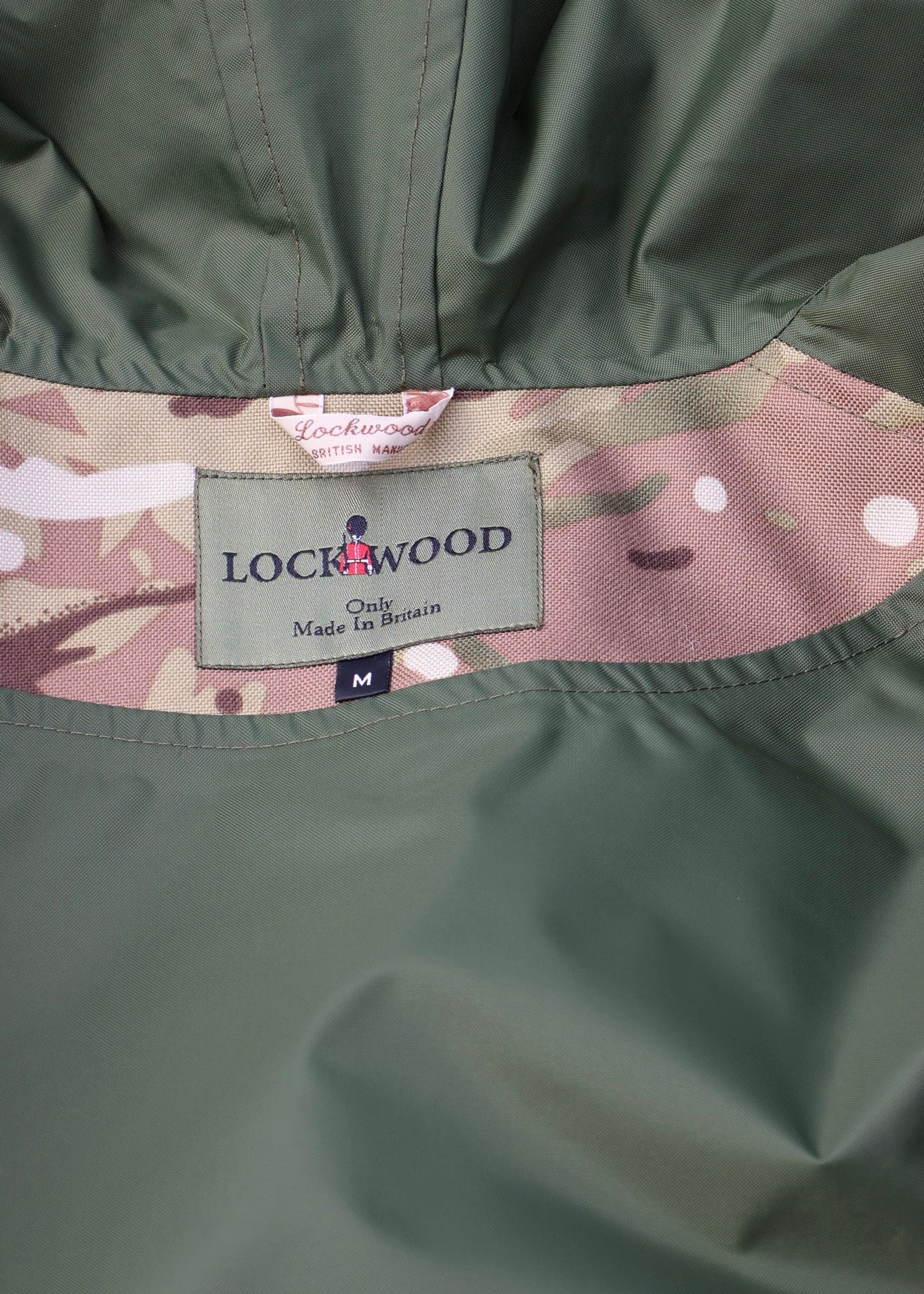 Close-up of a Lockwood jacket showing the olive green outer fabric, a camouflage inner lining, and the brand label.