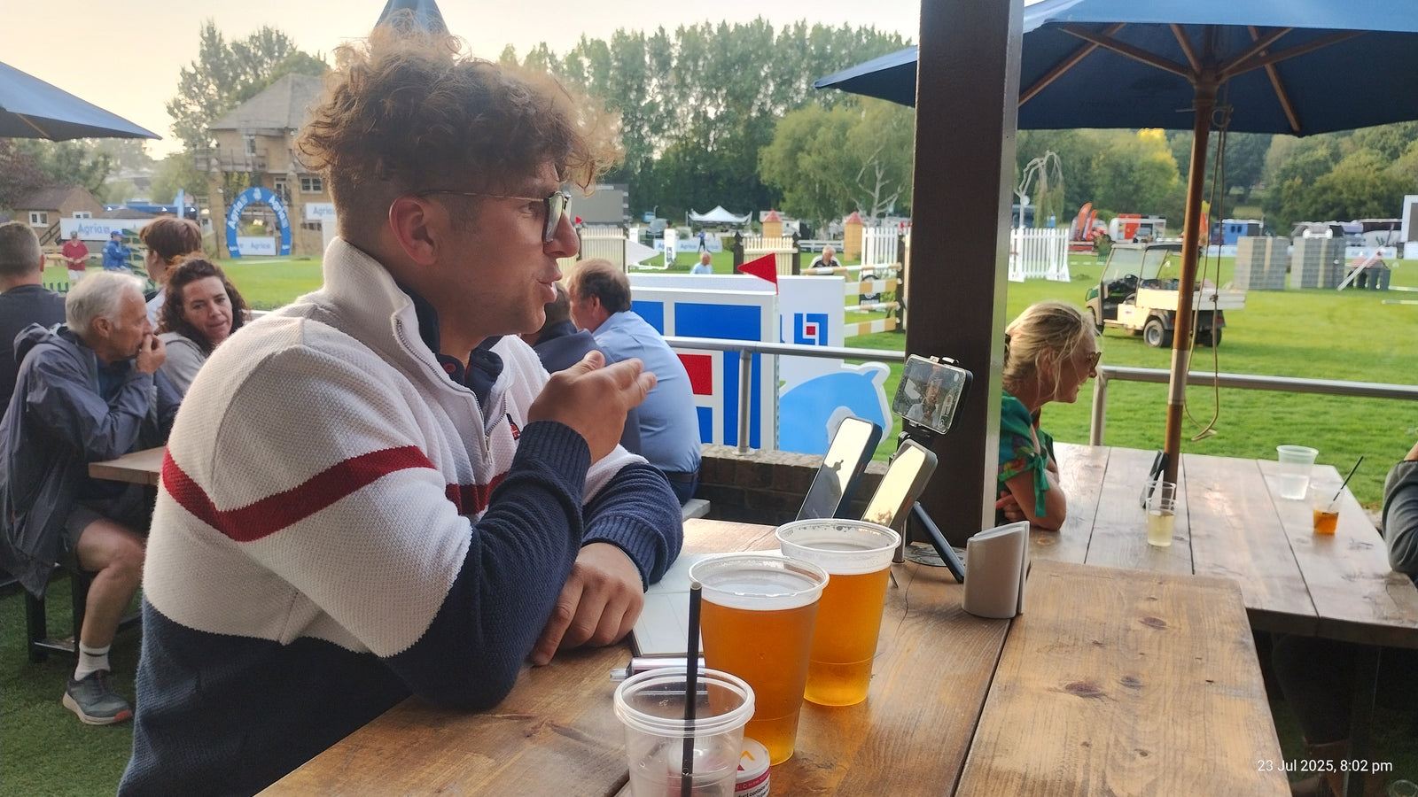 Man enjoying drinks outdoors at a bar with friends, surrounded by a lively atmosphere.