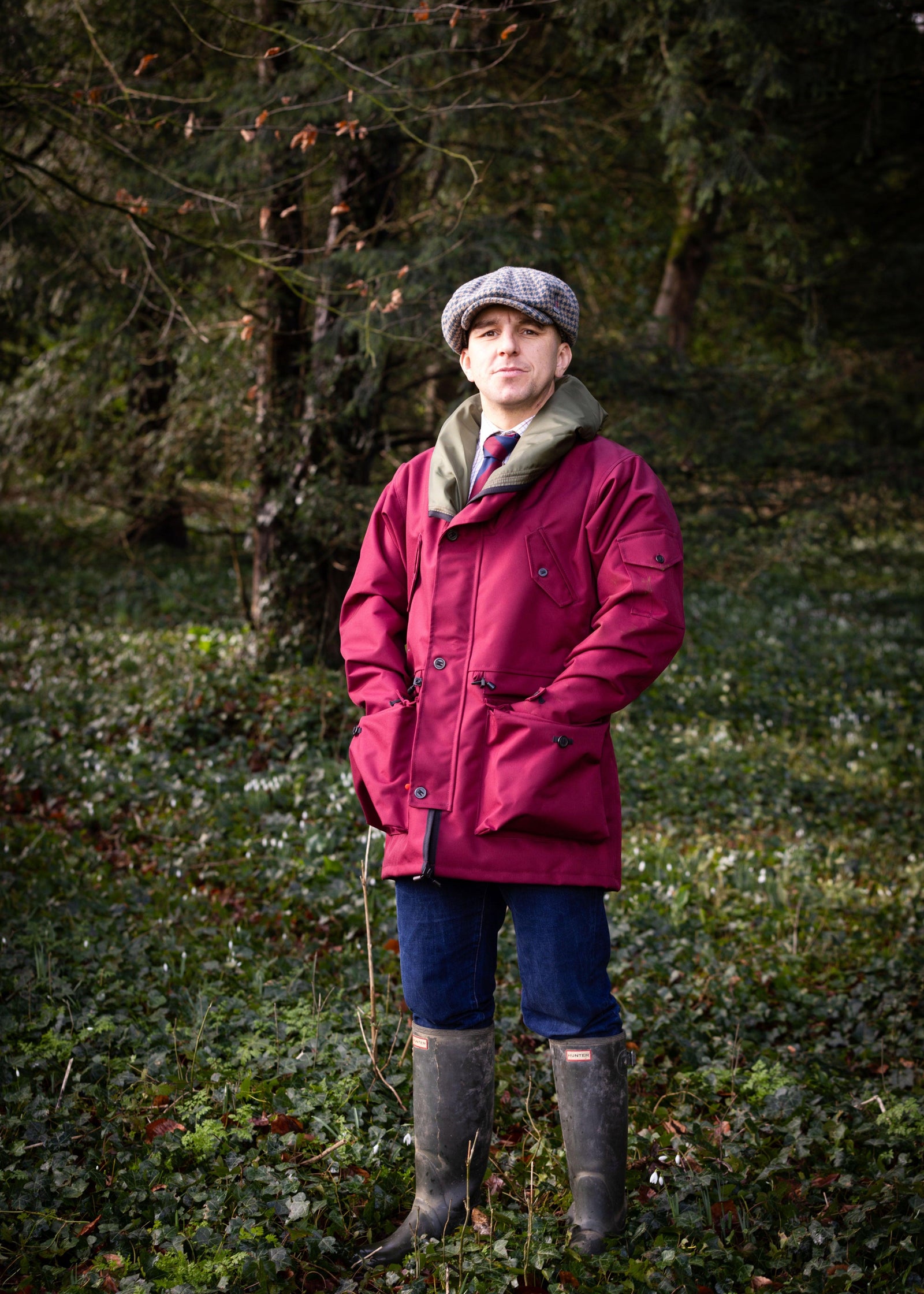 man stood in a woodland wearing a maroon waterproof jacket with the hood rolled