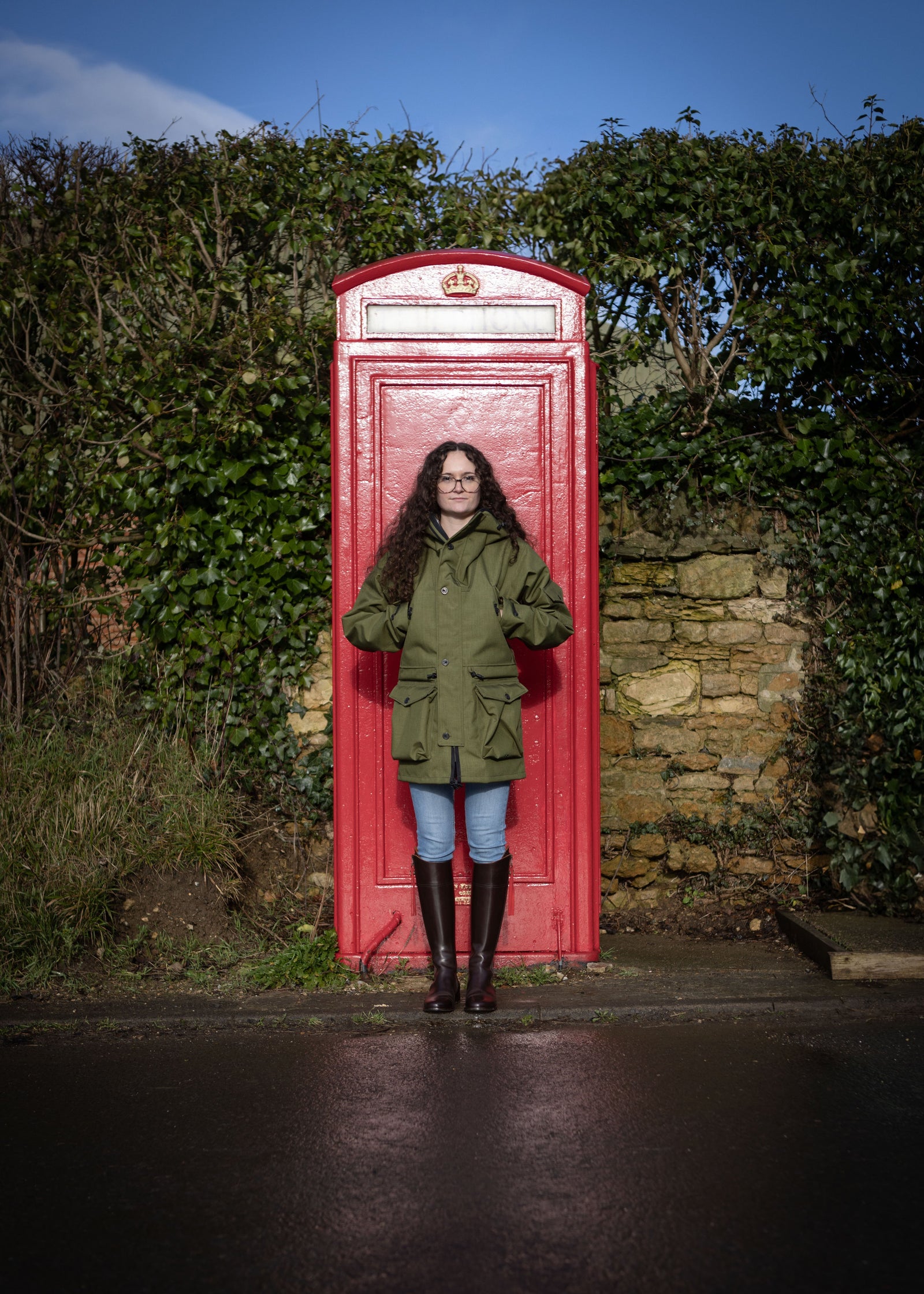 woman by telephone box wearing a green waterproof jacket with multiple pockets